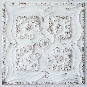 Op de afbeelding: Witte tinnen plafondtegel met een verweerde afwerking en een decoratief bloemmotief. De tegel heeft een reliëfdesign en een licht getextureerd oppervlak.