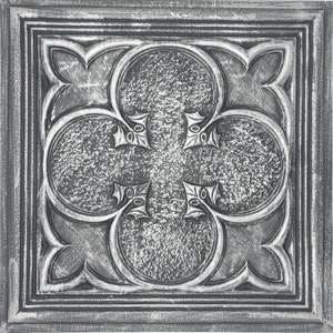 May include: A silver metal tile with a decorative quatrefoil design. The tile has a textured surface and a distressed finish.