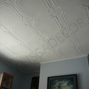 May include: White ceiling tiles with a decorative, raised, square pattern. The tiles are installed in a grid pattern. The ceiling is in a room with blue walls and a painting on the wall.