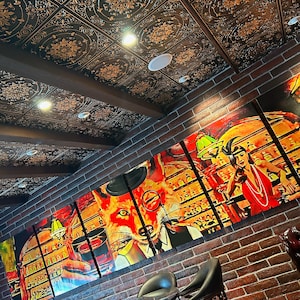 Op de afbeelding: Een bakstenen muur met een bar-thema muurschildering met een vos die een glas rode wijn vasthoudt. De muurschildering bestaat uit meerdere panelen. De muur is versierd met een zwart en gouden plafond met een decoratief patroon. Er staan drie zwarte leren barstoelen voor de muur.