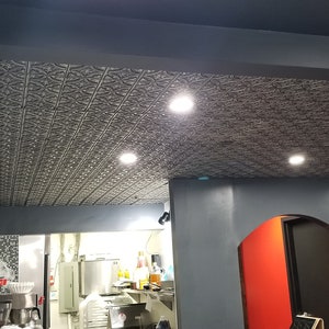 May include: A restaurant interior with a decorative tin ceiling, gray walls, and recessed lighting. A red Coca-Cola refrigerator is visible in the background.