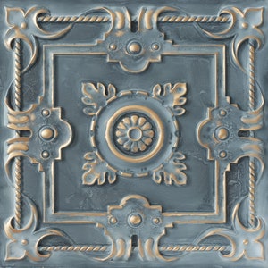 Op de afbeelding: Een decoratieve tegel met een blauw en gouden ontwerp. De tegel heeft een centraal bloemmotief omgeven door ingewikkelde krulwerk en touwachtige randen.
