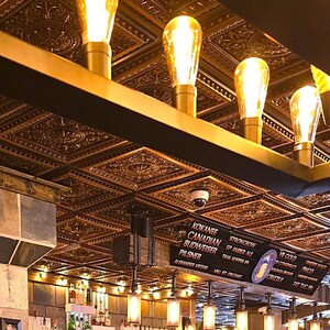 May include: A gold ceiling with decorative tile panels and a row of exposed light bulbs. The ceiling is illuminated by the light bulbs, creating a warm and inviting atmosphere. The ceiling is also decorated with a row of exposed light bulbs, which add to the industrial chic aesthetic.