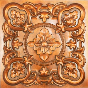 Könnte beinhalten: Eine dekorative Fliese mit einem komplizierten, verzierten Design in Kupferfarbe. Die Fliese zeigt ein zentrales Blumenmotiv mit wirbelnden, rollenartigen Mustern an den Rändern.