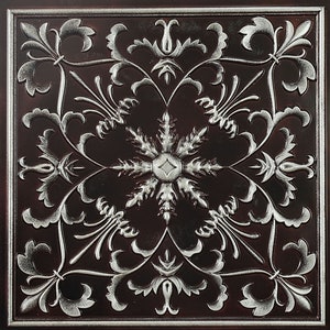 Könnte beinhalten: Eine dekorative Fliese mit einem silbernen floralen Design auf dunkelbraunem Hintergrund. Das Design zeigt ein zentrales Schneeflocke mit filigranen Details.