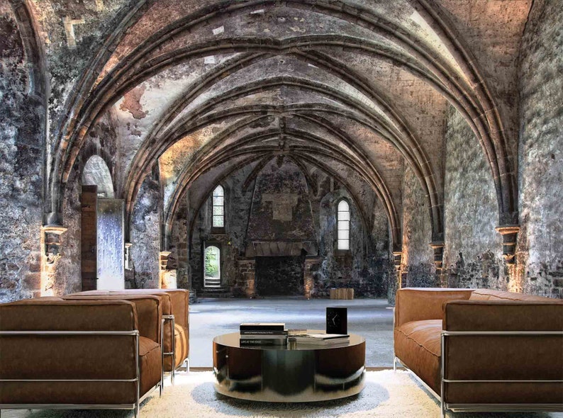 May include: Two brown leather sofas with metal frames sit facing each other in a large, vaulted room with stone walls. A round coffee table with a glass top sits between the sofas. The room has a high, arched ceiling and large windows.