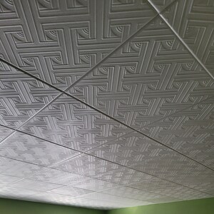 May include: White ceiling tiles with a geometric embossed pattern. The tiles are arranged in a grid pattern.