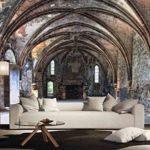 May include: A white sofa with pillows sits in front of a large stone archway with a vaulted ceiling. The archway is lit by natural light coming through windows in the stone walls. The room is empty except for the sofa and a coffee table.