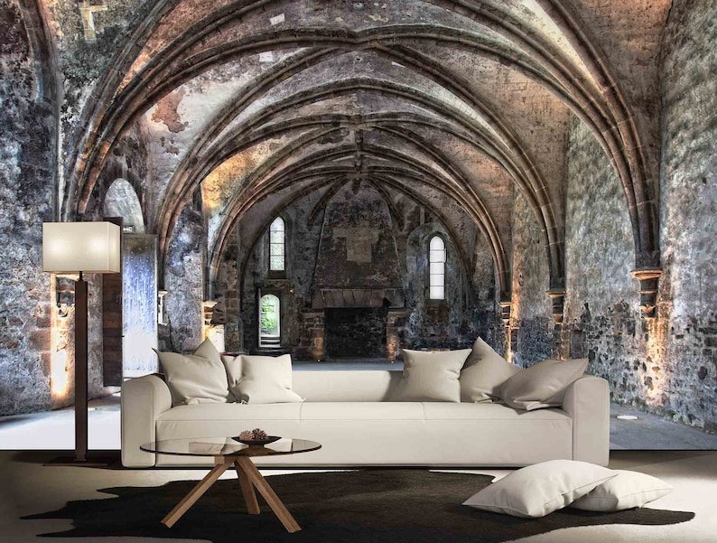 May include: A white sofa with pillows sits in front of a large stone archway with a vaulted ceiling. The archway is lit by natural light coming through windows in the stone walls. The room is empty except for the sofa and a coffee table.