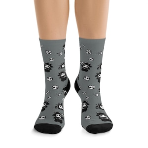 May include: A pair of gray socks with a black and white pattern of plague doctors and skulls. The socks are shown on a model's feet.