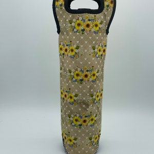 Peut inclure: Un porte-bouteille de vin beige avec une poignée noire. Le porte-bouteille présente un motif floral avec des tournesols jaunes et des cœurs blancs.