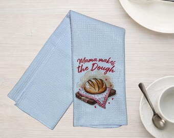 May include: Light blue waffle-weave kitchen towel with the text "Mama makes the Dough" in red script. The towel features a watercolor illustration of a loaf of bread on a wooden cutting board with a pink and white patterned cloth.