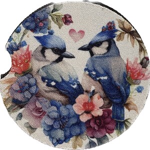 Puede incluir: Un posavasos con un par de pájaros azules con detalles florales. Los pájaros están posados en una rama con flores rosas, rojas y moradas. El fondo es una tela de color crema con una textura sutil.