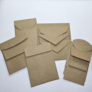May include: A collection of various sized brown paper envelopes. The envelopes have different flap designs, including rounded and rectangular shapes. The paper has a natural, unbleached appearance, suggesting a rustic or eco-friendly aesthetic.