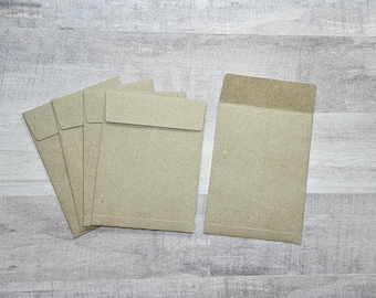 May include: Five brown paper envelopes with a flap on the top. The envelopes are stacked on top of each other. The envelopes are on a light wood surface.
