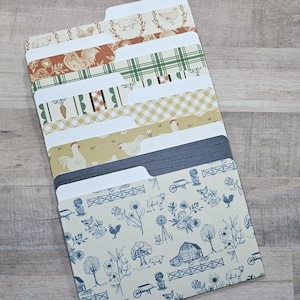 May include: A set of six stacked file folders featuring various patterns including farm animals, chickens, carrots, plaid, and gingham in shades of blue, green, yellow, and brown. Each folder has a tab at the top for organization and labeling.