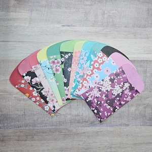 May include: A collection of colorful paper envelopes fanned out on a wooden surface. Each envelope features a unique floral pattern in shades of pink, purple, blue, and green. The envelopes are arranged in a semi-circle, showcasing their diverse designs.