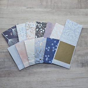 May include: A collection of rectangular paper envelopes arranged in a fan shape. The envelopes feature various patterns including floral prints, geometric gold foil lines, solid pastel colors, and intricate damask designs in shades of blue, pink, and gray.