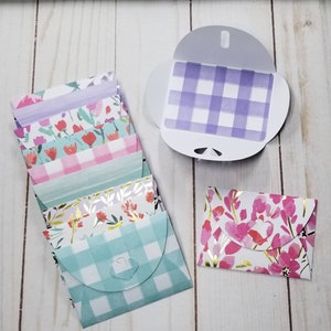 May include: A stack of six small envelopes with different floral and checkered patterns. The envelopes are folded and ready to be used for sending notes or small gifts.