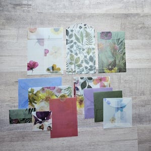 May include: Assortment of small, colorful envelopes with floral designs. The envelopes are made of translucent paper with pressed flowers and leaves.