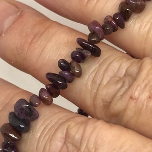 May include: A purple gemstone bracelet with small, irregular shaped beads. The bracelet is made of natural stones and is approximately 7 inches in length.