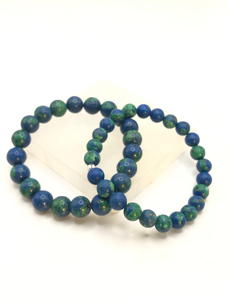 K&ouml;nnte beinhalten: Zwei blaue und gr&uuml;ne Edelstein-Armb&auml;nder mit silbernen Verschl&uuml;ssen. Die Armb&auml;nder bestehen aus runden Perlen und sind &uuml;bereinander gestapelt.