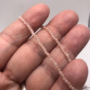 May include: A strand of pale pink gemstone beads, strung on a thin wire. The beads are small and round, and the strand is about 18 inches long.