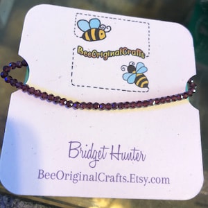 May include: A purple crystal beaded bracelet on a white card with the text "BeeOriginalCrafts.Etsy.com" and "Bridget Hunter".
