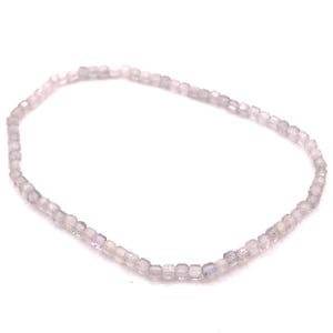 May include: A delicate bracelet composed of small, light-colored, square-cut beads. The beads are strung together, forming a flexible chain. The bracelet is displayed against a white background, highlighting its subtle color and design.