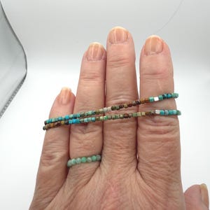 May include: A double-wrap bracelet composed of small, square-shaped turquoise and brown beads with a single silver-toned accent bead, paired with a separate ring featuring a single band of small, round, light green beads.