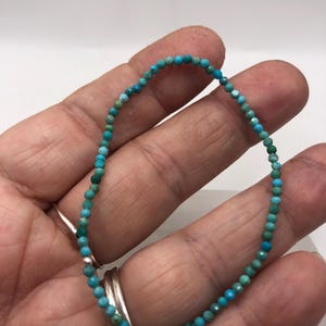 May include: A delicate turquoise beaded bracelet. The bracelet is composed of small, round, faceted turquoise beads strung together. The beads display a range of blue-green hues. The bracelet is shown against a neutral background.