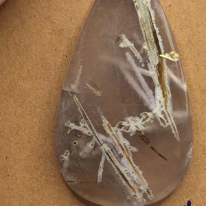 May include: A teardrop-shaped pendant with a clear, translucent stone featuring a unique pattern of white and brown inclusions. The pendant is attached to a silver bail.