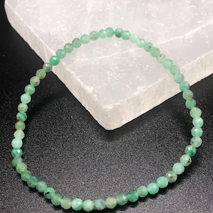 May include: A green gemstone bracelet made of small, faceted beads. The bracelet is on a white surface.