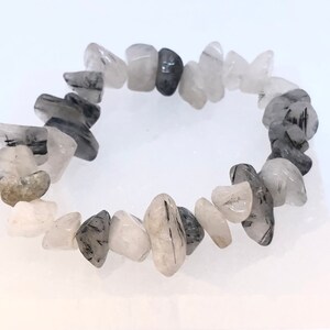 May include: A bracelet made of clear quartz stones with black tourmaline inclusions. The stones are irregularly shaped and have a natural, raw look.