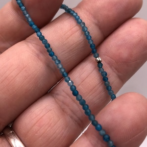 Op de afbeelding: Een streng blauwe edelsteen kralen met een zilveren kraal accent. De kralen zijn klein en rond, en de streng is ongeveer 45 cm lang.