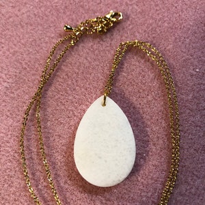 May include: A white teardrop-shaped pendant necklace with a gold chain.