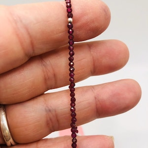 May include: A delicate bracelet made with small, faceted, dark red garnet beads and silver spacer beads.