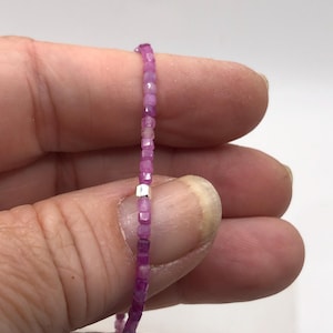 May include: A fine beaded necklace composed of small, square-cut pink gemstones. The necklace is strung on a thin, almost invisible cord, with a small silver-coloured spacer bead. The gemstones are a vibrant shade of pink.