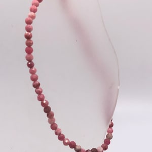 May include: A pink gemstone bracelet made with small, faceted beads. The bracelet is strung on a thin, clear elastic cord.