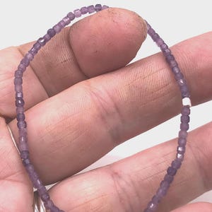 Puede incluir: Una delicada pulsera de cuentas con pequeñas cuentas púrpuras translúcidas y facetadas ensartadas en un bucle circular continuo. El diseño incluye una única cuenta espaciadora pequeña de tono plateado metálico entre las cuentas.