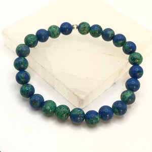 K&ouml;nnte beinhalten: Ein blaues und gr&uuml;nes Edelstein-Armband mit einem silbernen Verschluss. Das Armband besteht aus runden Perlen.