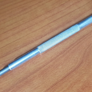 Puede incluir: Una herramienta de metal plateado con una punta de goma negra y un agarre texturizado.