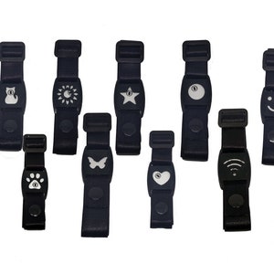 Puede incluir: Una colección de correas negras ajustables con varios iconos blancos, incluyendo un gato, sol, estrella, símbolo del yin-yang, cara sonriente, perro, huella de pata, mariposa, corazón y símbolo Wi-Fi. Las correas tienen un cierre de hebilla.