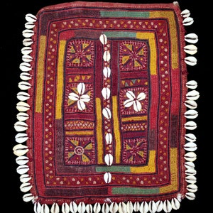 May include: A red fabric square with a geometric pattern embroidered in colorful threads. The fabric is trimmed with a row of white seashells.