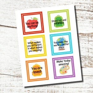 May include: A white sheet of paper with six colorful square designs, each with a motivational message. The designs include an apple, backpack, globe, and paint palette, with phrases like "You can be anything!" and "Make today amazing!"