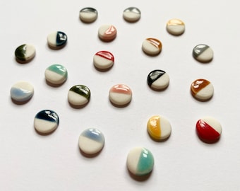 May include: A collection of 19 small, round ceramic tiles with a white base and a colored half-circle design. The colors include red, blue, green, yellow, black, and brown.