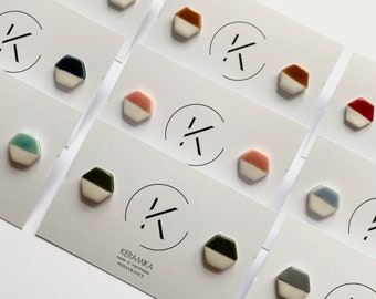 May include: Assortment of ceramic hexagon earrings in various colors, including blue, green, yellow, pink, red, brown, and black. Each earring has a white base and a colored top. The earrings are displayed on white cards with the word "KERAMIKA" printed on one card.
