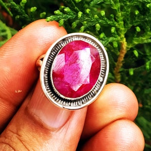 Op de afbeelding: Een zilveren ring met een grote, ovale, gefacetteerde robijn. De robijn is diep rood van kleur.
