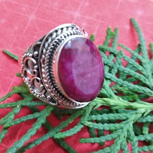 May include: A silver ring with an oval-shaped, deep pink gemstone set in a detailed silver band.