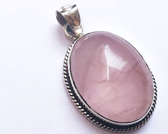 May include: A silver pendant with a large oval-shaped pink rose quartz gemstone. The pendant has a detailed silver border.